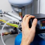 Hand adjusting water filtration system control panel, showcasing plumbing installation for improved water quality and filtration efficiency.